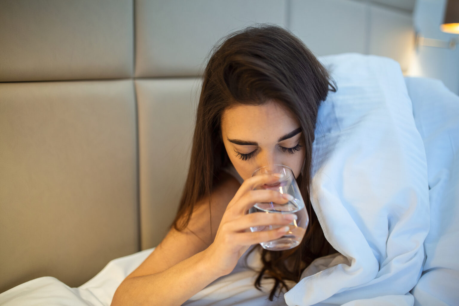 Persona bebiendo agua mientras permanece recostada en la cama durante la noche.