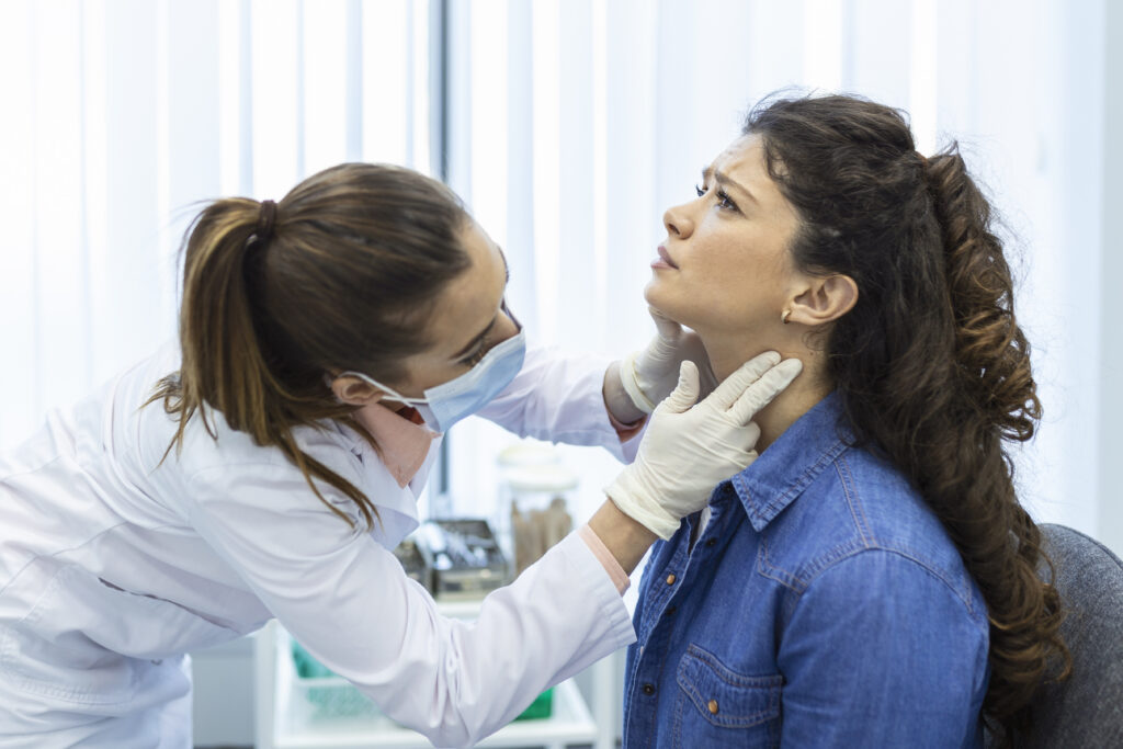 Persona durante una consulta médica por afonía mientras un especialista examina la zona de la garganta y el cuello.